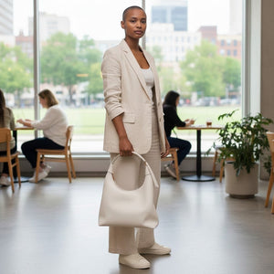 Mujer con traje de lino beige sosteniendo un bolso Xava BE XAVAGE blanco de diseño minimalista en una oficina moderna.