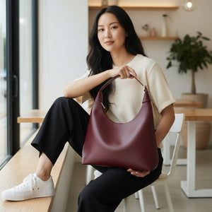 Mujer joven sosteniendo un bolso Xava BE XAVAGE color burdeos de diseño minimalista y elegante en un entorno moderno.