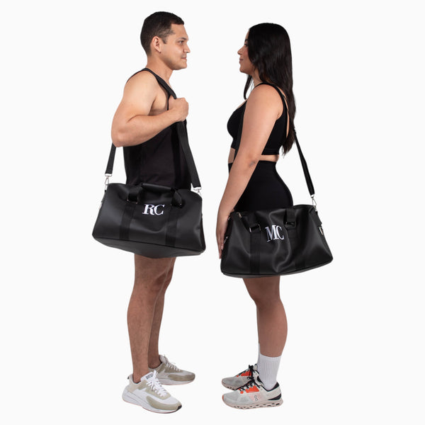 Bolso deportivo/viajero unisex , Xava Go en color negro con iniciales personalizadas, llevado por un hombre y una mujer.