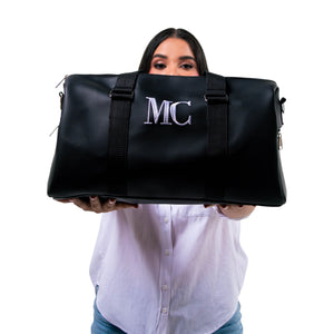 Bolso unisex Xava Go negro de material perforado con iniciales bordadas, sostenido por una mujer frente a su rostro.
