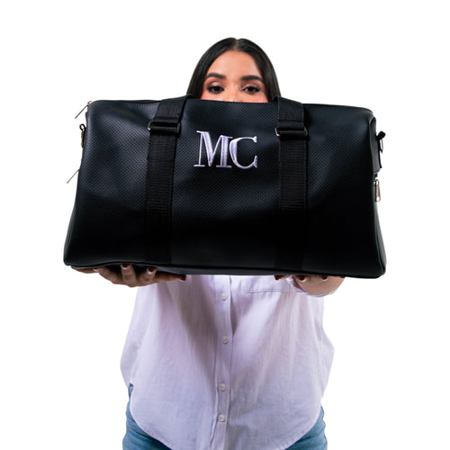 Bolso unisex Xava Go negro de material perforado con iniciales bordadas, sostenido por una mujer frente a su rostro.