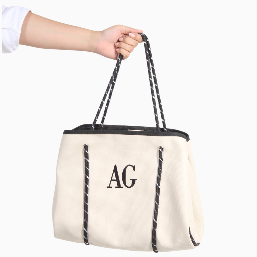Bolso grande Xava negro de material sintético con textura perforada, iniciales bordadas y tirantes de cuerda gráfica.